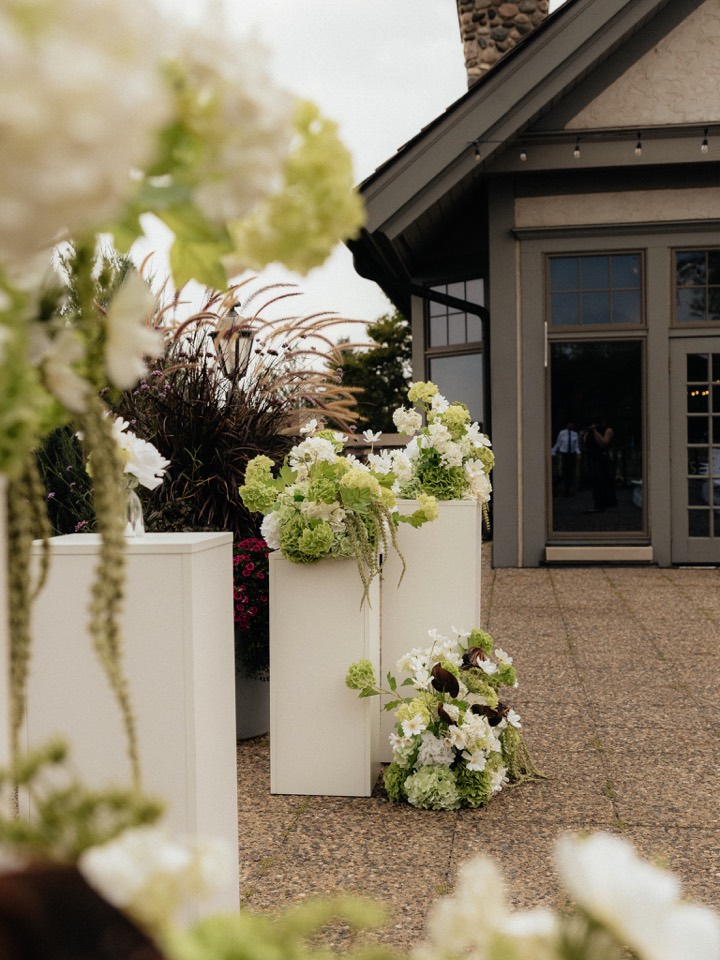 White pedestal arrangements of hydrangea and white blooms at an outdoor ceremony