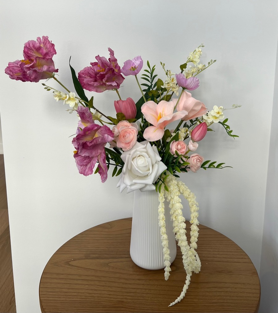 Standard spring arrangement: pink and blush blooms, a white rose and trailing amaranthus in a white fluted vase