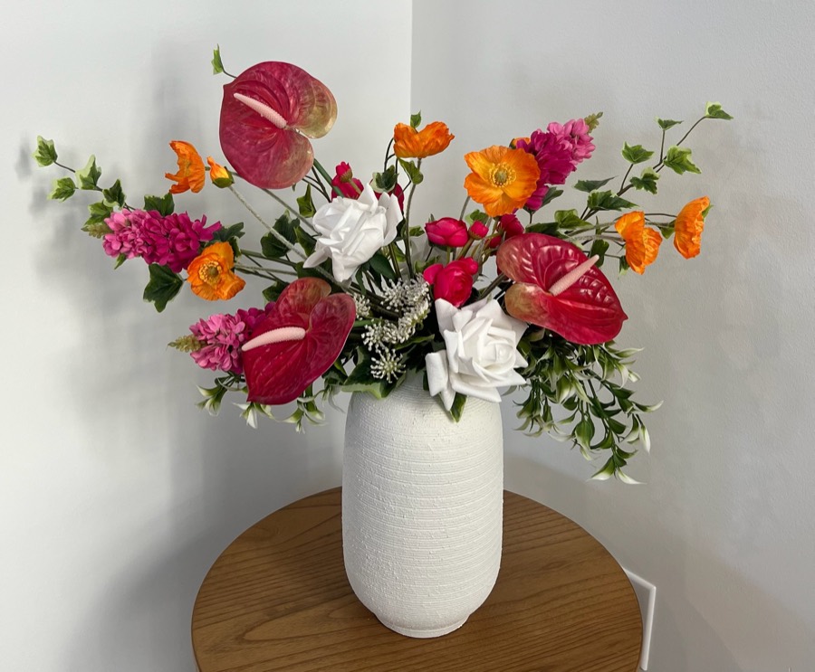 Premium summer arrangement: a fuller arrangement of orange poppies, magenta blooms, white roses and red anthuriums in a white textured vase