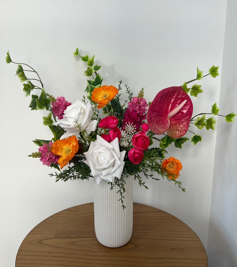 Standard summer arrangement: orange poppies, magenta blooms, white roses and a pink anthurium in a white fluted vase